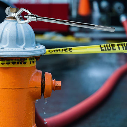 Orange fire hydrant with a wrench on top, surrounded by caution tape, with a blurred background.