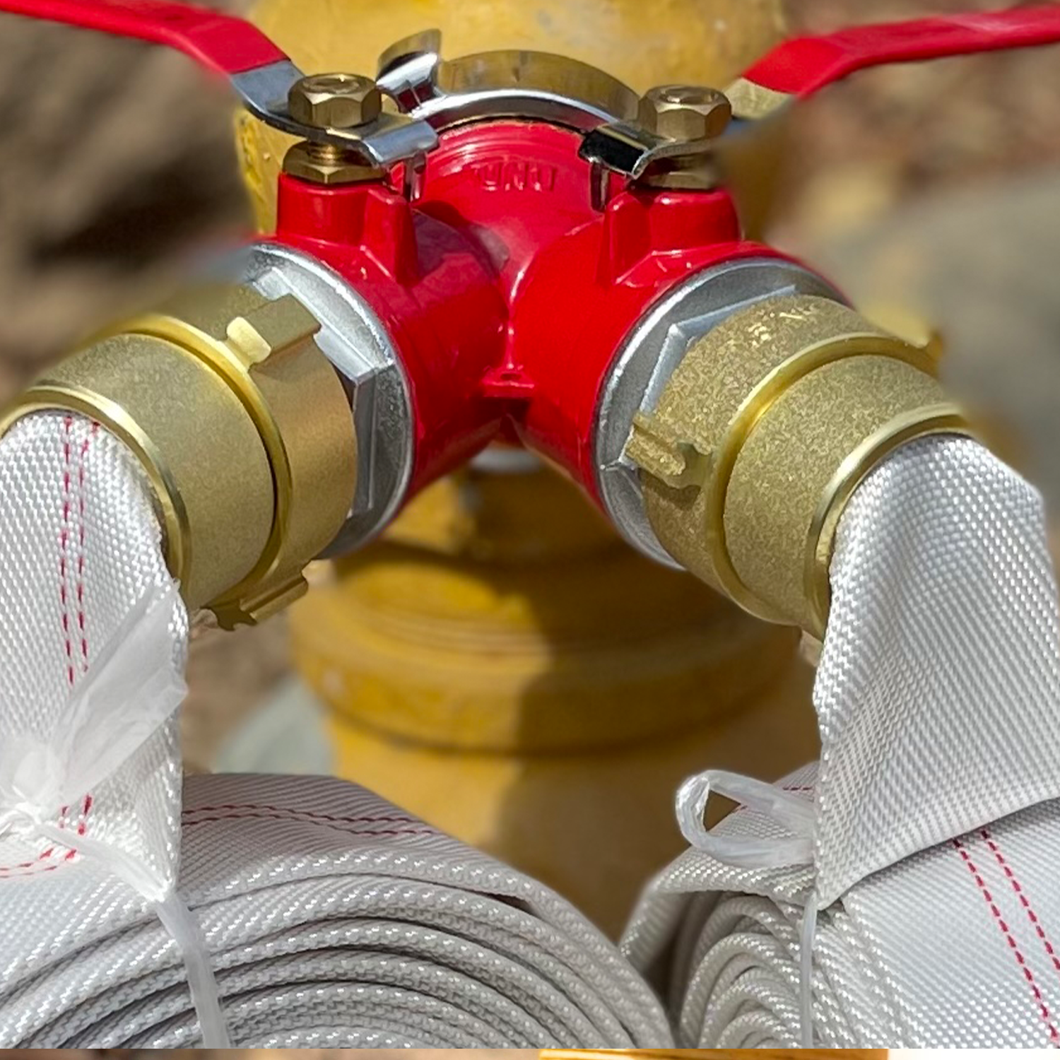 Brass Wye fitting Fire Hydrant Splitter Gated Valve Red and gold fire hose nozzle with white hoses on a blurred background