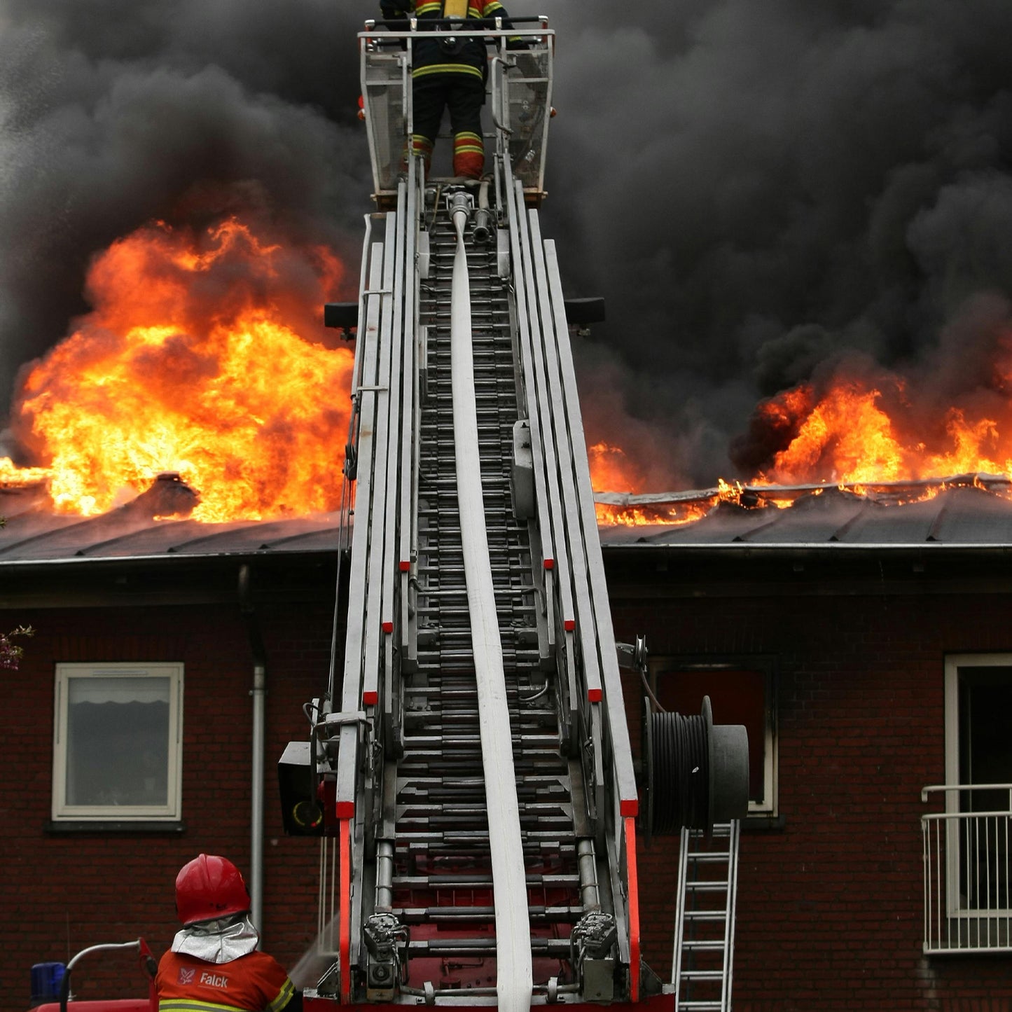 Firefighters using a ladder to combat a fire on a building with flames and smoke.